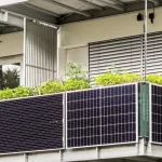 Balkonkraftwerk mit mehreren schwarzen Solarmodulen vor einem Einfamilienhaus auf einer Rasenfläche.