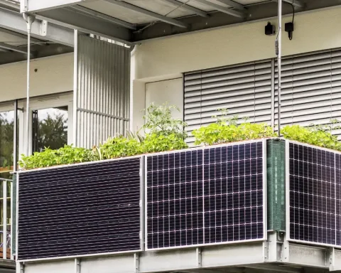 Balkonkraftwerk mit mehreren schwarzen Solarmodulen vor einem Einfamilienhaus auf einer Rasenfläche.